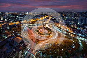 Aerial view of Victory Monument with car light trails on busy street road. Roundabout in Bangkok Downtown Skyline. Thailand.