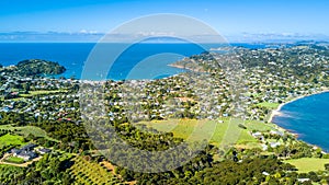 Aerial view on a vineyard on the shore of sunny harbour with residential suburbs on the background. Waiheke Island, New Zealand