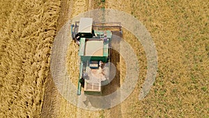 Aerial view of vintage combine harvesting wheat in field. Flying directly above agricultural machine