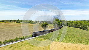 Aerial view of a vintage steam train traveling through a vast rural landscape, with plowed and green fields