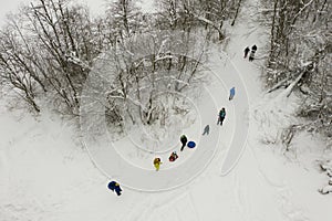 Aerial view on walking people with children on snow tubing and sladges on the forest pathway. Parents with children, snow fun