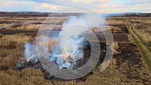 Aerial view of waste pile burning with red fire on grassland field during dry season. Natural disaster and climate