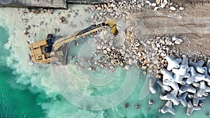 Aerial view of waterfront construction site with excavator. Excavator working on a breakwater construction