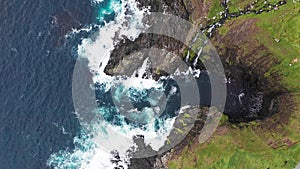 Aerial view of waves break on rocks of Faroe islands cliffs in a blue ocean.Drone Aerial Footage of green nature and the