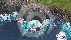 Aerial view of waves break on rocks of Faroe islands cliffs in a blue ocean.Drone Aerial Footage of green nature and the