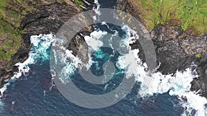 Aerial view of waves break on rocks of Faroe islands cliffs in a blue ocean.Drone Aerial Footage of green nature and the