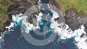 Aerial view of waves break on rocks of Faroe islands cliffs in a blue ocean.Drone Aerial Footage of green nature and the