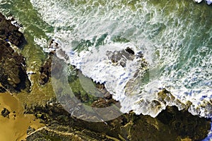 Aerial view of waves breaking on rocks and then moving out to a green sea