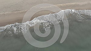 Aerial view of waves crashing on the shore with foam and undertow