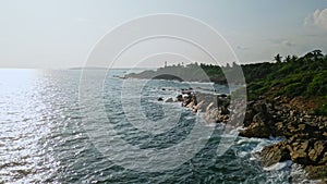 Aerial view of waves hitting rocky shore near hilltop lighthouse. Scenic coastline panorama for mariners, tourists
