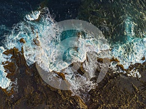 Aerial view of waves and sea crashing over volcanic coastline rocks