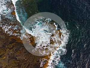 Aerial view of waves and sea crashing over volcanic coastline rocks