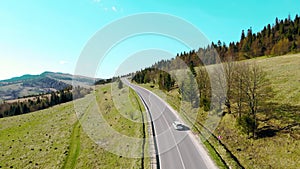 Aerial view white car travels in beautiful mountainous terrain. One car driving on an asphalt road with a beautiful