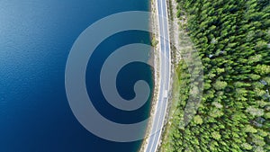 Aerial view of white caravan car driving on country road in forest near lake