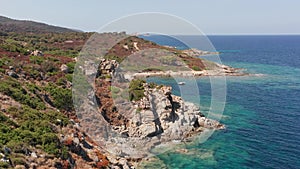 Aerial view of white rock, hills with arid vegetation, sand beach, waves crushing on the beach. Colored sea, blue