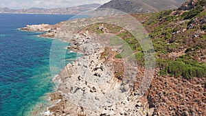 Aerial view of white rock, hills with arid vegetation, sand beach, waves crushing on the beach. Colored sea, blue