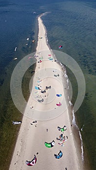 Aerial view of white sand beach peninsula with kites for kite surfing laying down on the beach and some kite surfers flying on the