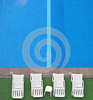 Aerial view of white sunbeds at the side of a blue swimming pool with bright water and a stripe in the tiles