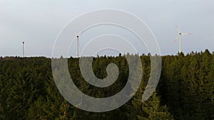 Aerial view of wind farm turbines set up in countryside with forest. Producing power using energy of nature