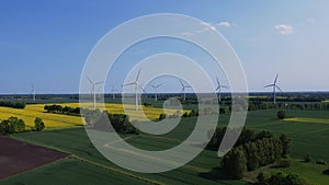 Aerial view Wind turbine on grassy yellow farm canola field against cloudy blue sky in rural area. Offshore windmill