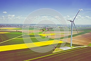 Aerial view of wind turbine. Rapeseed blooming. Windmills and yellow fields from above. Agricultural fields on a summer day.