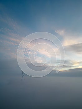 Aerial view of wind turbines or windmills farm field in industry factory with fog. Power, sustainable green clean energy