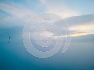 Aerial view of wind turbines or windmills farm field in industry factory with fog. Power, sustainable green clean energy