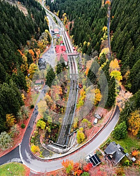 Aerial view of a winding rural road and train tracks, running through a dense forest in autumn