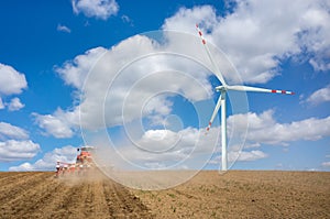 Aerial view on the windmill and the tractor harrowing the field