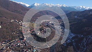 Aerial view of winter Austria village in the valley near picturesque sunny Alp mountains. Clip. Flying over the roads