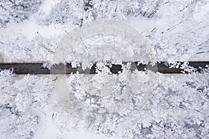 Aerial view of winter beautiful landscape road with trees covered with hoarfrost and snow. Winter scenery from above. Landscape