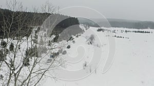 Aerial view of winter coniferous forest. Clip. snow falling on a rural road with parked cars near snow covered white