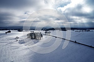 Aerial view of a winter curved road covered with snow. A snowy plateau with single trees captured from above with a