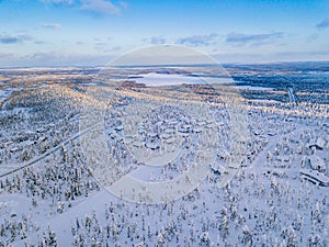 Aerial view of winter forest with frosty trees, rural road and village in Finland