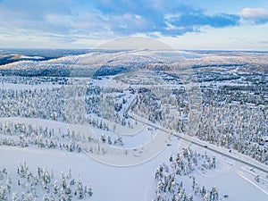 Aerial view of winter forest with frosty trees, rural road and village in Finland