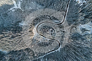 Aerial view of winter landscape with snow covered mountain hills and winding forest road in morning