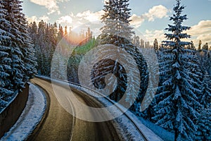 Aerial view of winter landscape with snow covered mountain hills and winding forest road in morning