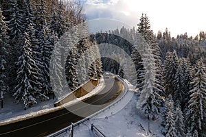Aerial view of winter landscape with snow covered mountain hills and winding forest road in morning