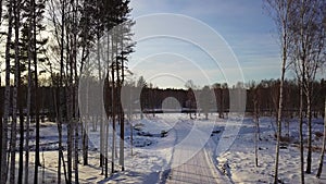 Aerial view of winter landscape with snow covered road. Action. Flying along rare trees towards the forest and blue