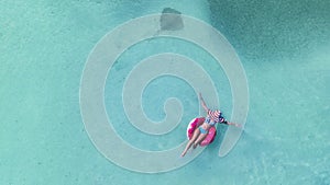 Aerial view with woman in bikini sunbathing as laying on swim ring as blue sea water i