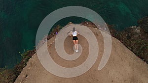 Aerial view of woman exercising on sea shore cliff at sunrise