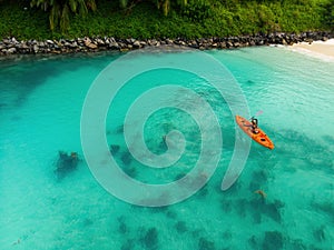 Aerial view of woman kayaking in a lagoon in Mahe, Seychelles. Top view of woman floating on orange kayak near a tropical beach