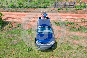 Aerial view of a woman and a man on the back of a pick-up truck in Paraguay with typical red sand path.