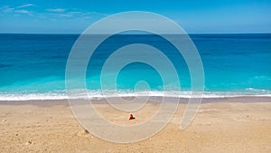 Aerial view of woman in red dress sitting on the sandy beach with a baby, enjoying soft turquoise ocean wave. Tropical sea in