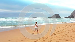 Aerial view of woman running along sandy beach with sea waves
