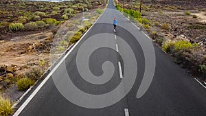 Aerial view of the woman runs along the deserted asphalt road at sunset, back view. Mountains on the background