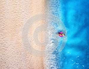 Aerial view of a woman with swim ring in blue sea, sandy beach
