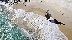 Aerial view of woman walking on the sandy beach with ocean waves braking on the coast