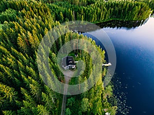 Aerial view of wooden cottage in green forest by the blue lake in rural summer Finland