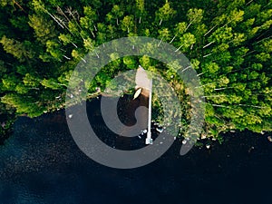 Aerial view of wooden pier with fishing boat on blue lake with green forest in Finland